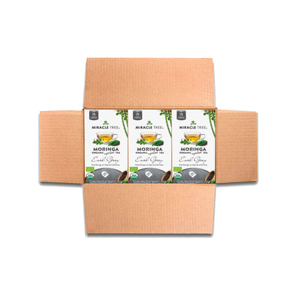 A cardboard box opens to reveal four packs of Miracle Tree Organic Moringa Tea, Earl Grey. The white packaging features images of a teacup, vibrant green moringa leaves, and brand logos.