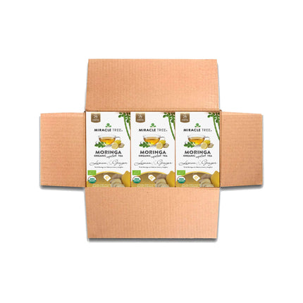 A cardboard box opens to reveal four boxes of Miracle Trees Organic Moringa Tea, Lemon & Ginger. This caffeine-free superfood tea features lemons, ginger, and green leaves on its packaging.
