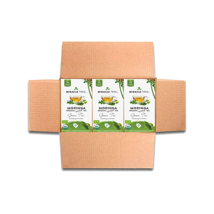 An open cardboard box contains three packages of Miracle Tree Organic Moringa Tea, Green Tea. Each package displays a steaming teacup and leaves on a white background, highlighting the benefits of this superfood tea.