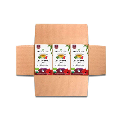 An open brown cardboard box reveals Miracle Tree tea packages containing nutrient-rich Organic Moringa Tea, Hibiscus, adorned with vibrant hibiscus and tea leaf illustrations.