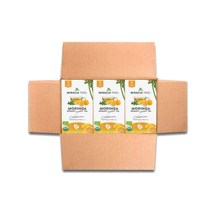 An open box displays three packages of Miracle Trees Organic Moringa Tea, Lemon flavor. Each caffeine-free package features vibrant images of lemons, ginger roots, and various certification symbols.