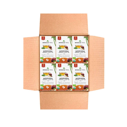 Open cardboard box with multiple Miracle Tree brand Organic Moringa Tea boxes. The primarily white packaging features green text and leaf images, highlighting its apple & cinnamon flavor.