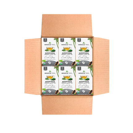 An open cardboard box contains six Miracle Tree Organic Moringa Tea, Earl Grey packets, each featuring green leaves and a teacup on the label to highlight its superfood benefits. The packaging shows organic and non-GMO certifications, all viewed from above against a white background.