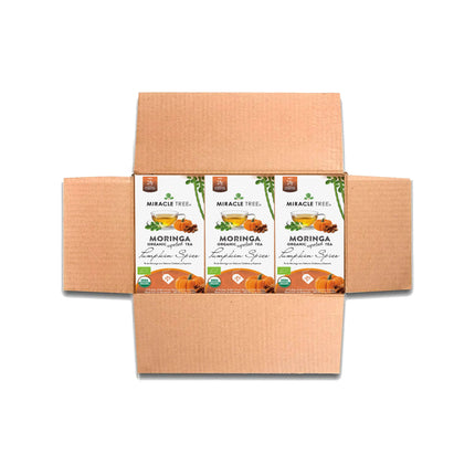An open cardboard box shows four packs of Miracle Trees Organic Moringa Tea, Pumpkin Spice. The packages feature green and orange accents with images of moringa leaves and pumpkins, highlighting its caffeine-free superfood blend.