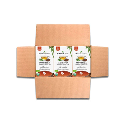 Open cardboard box with three packages of Miracle Tree Organic Moringa Tea, Rooibos. Each package, labeled as a nutrient-dense superfood, features moringa leaf tea. The green and white packaging highlights the product as a wellness essential.