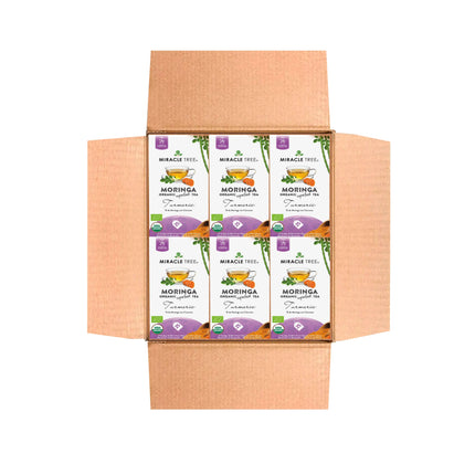 An open cardboard box displays six white boxes of Miracle Trees Organic Moringa Tea, Turmeric flavor. Each box, decorated with green and purple designs and a tea cup image, highlights the vibrant appeal of this superfood.