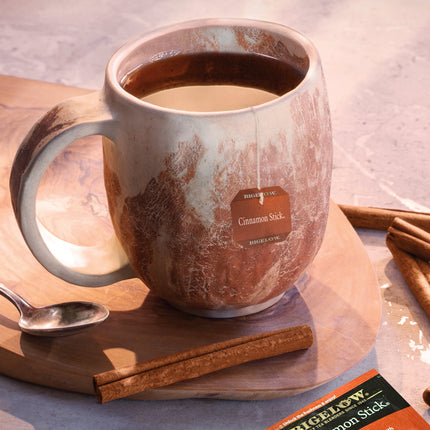 Mug of hot tea with a Bigelow Cinnamon Stick tea bag on a wooden board.